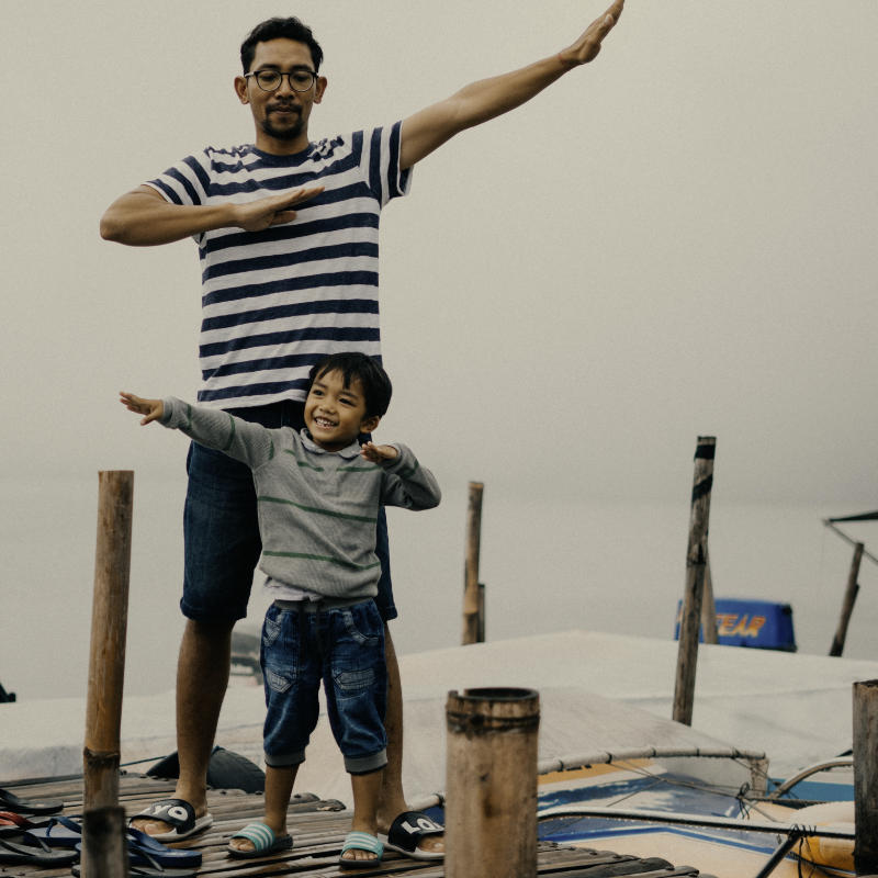 Vater und Sohn posieren fröhlich am Wasser, umgeben von einer malerischen Kulisse.